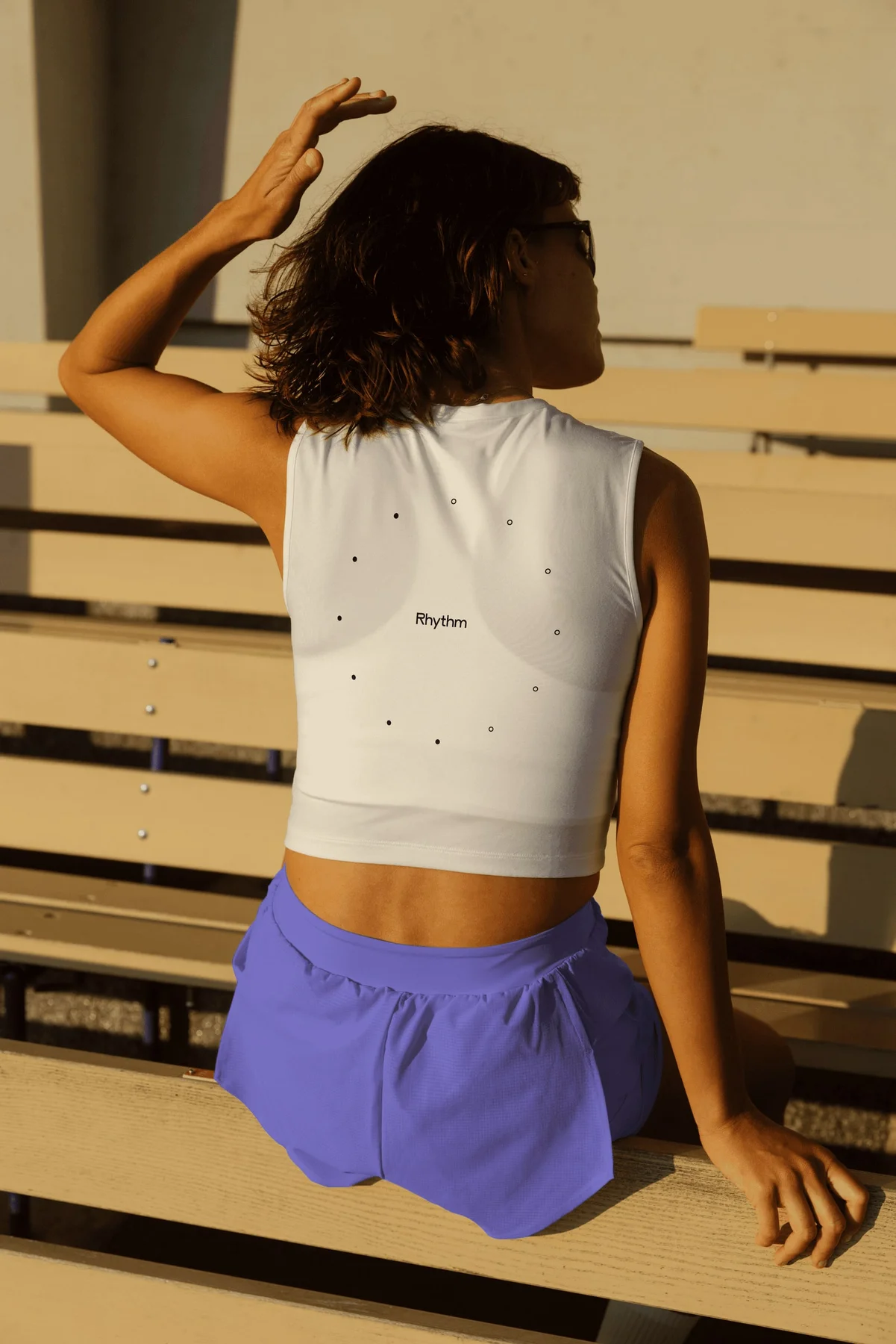 Person wearing a white cropped Rhythm top and purple shorts.