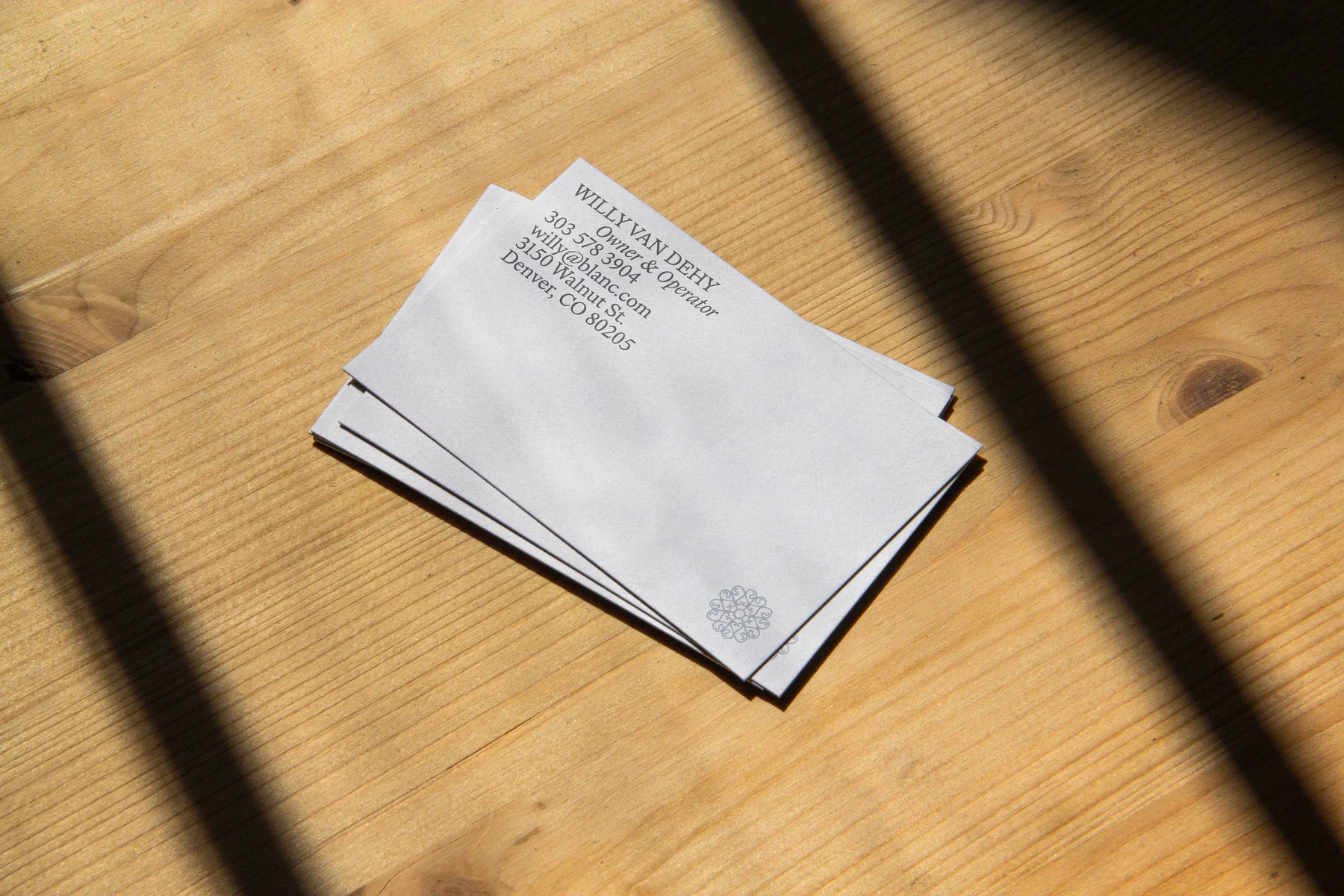 White Blanc printed cards on a sunlit wooden table.