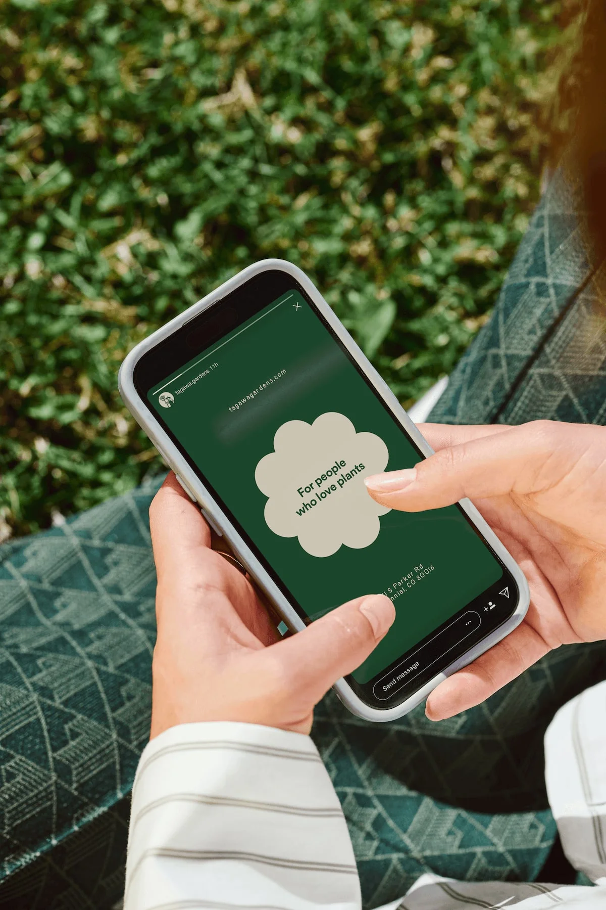 Tagawa Gardens mobile website on a phone held among plants.