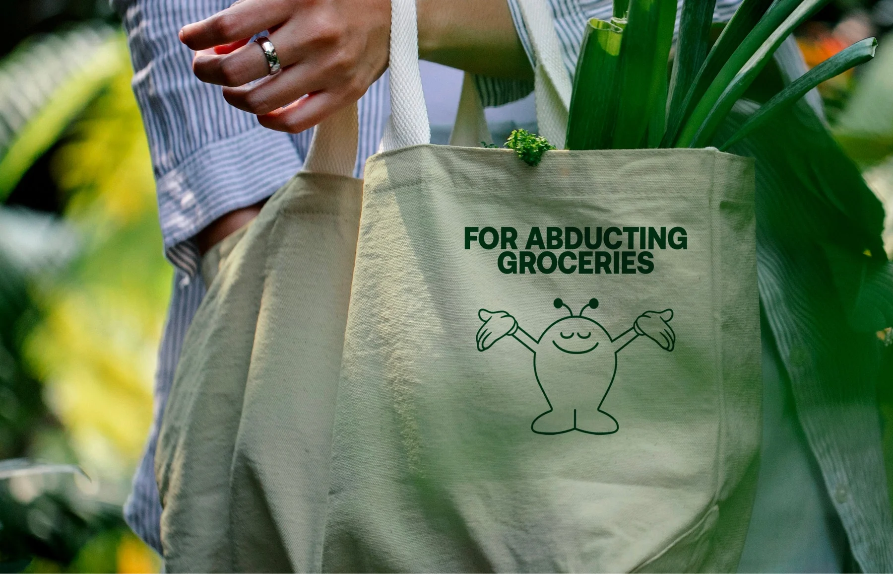 Green Nomad tote bag with a character and For Abducting Groceries lettering.