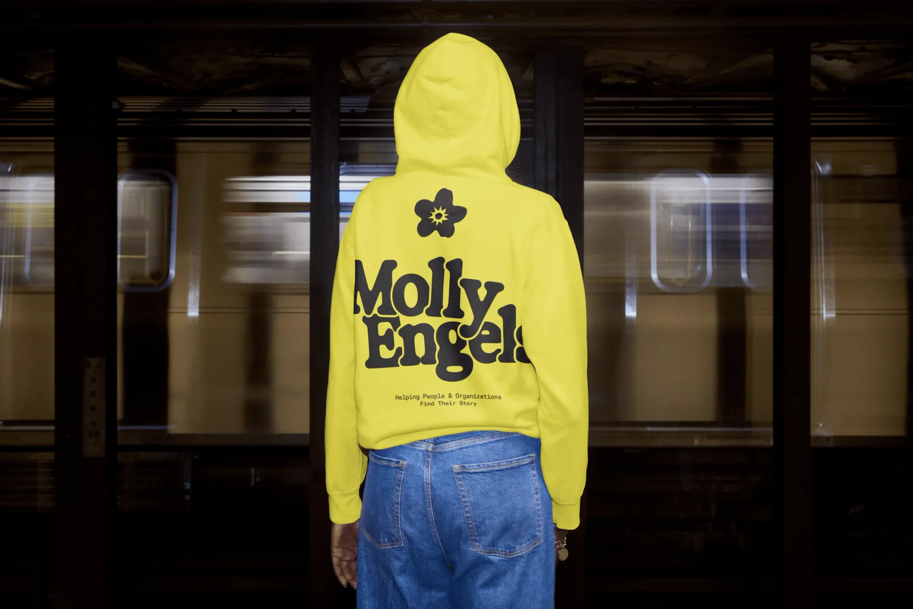Person wearing a yellow Molly Engels hoodie in a subway station.