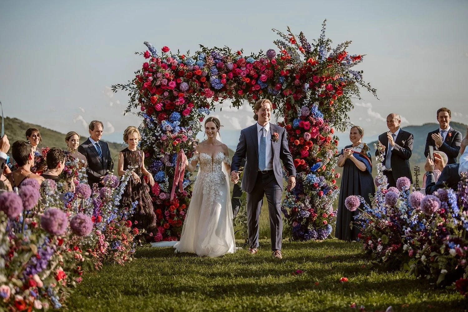 Wedding party beneath a colorful floral arch.