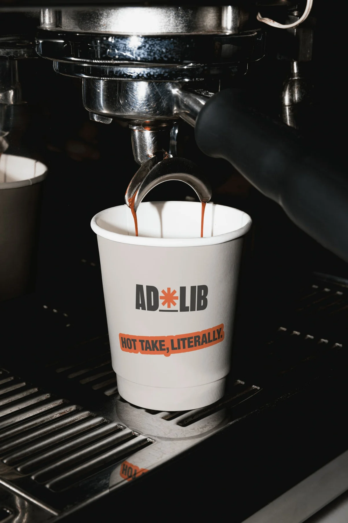 AdLib takeaway cup beneath an espresso machine.