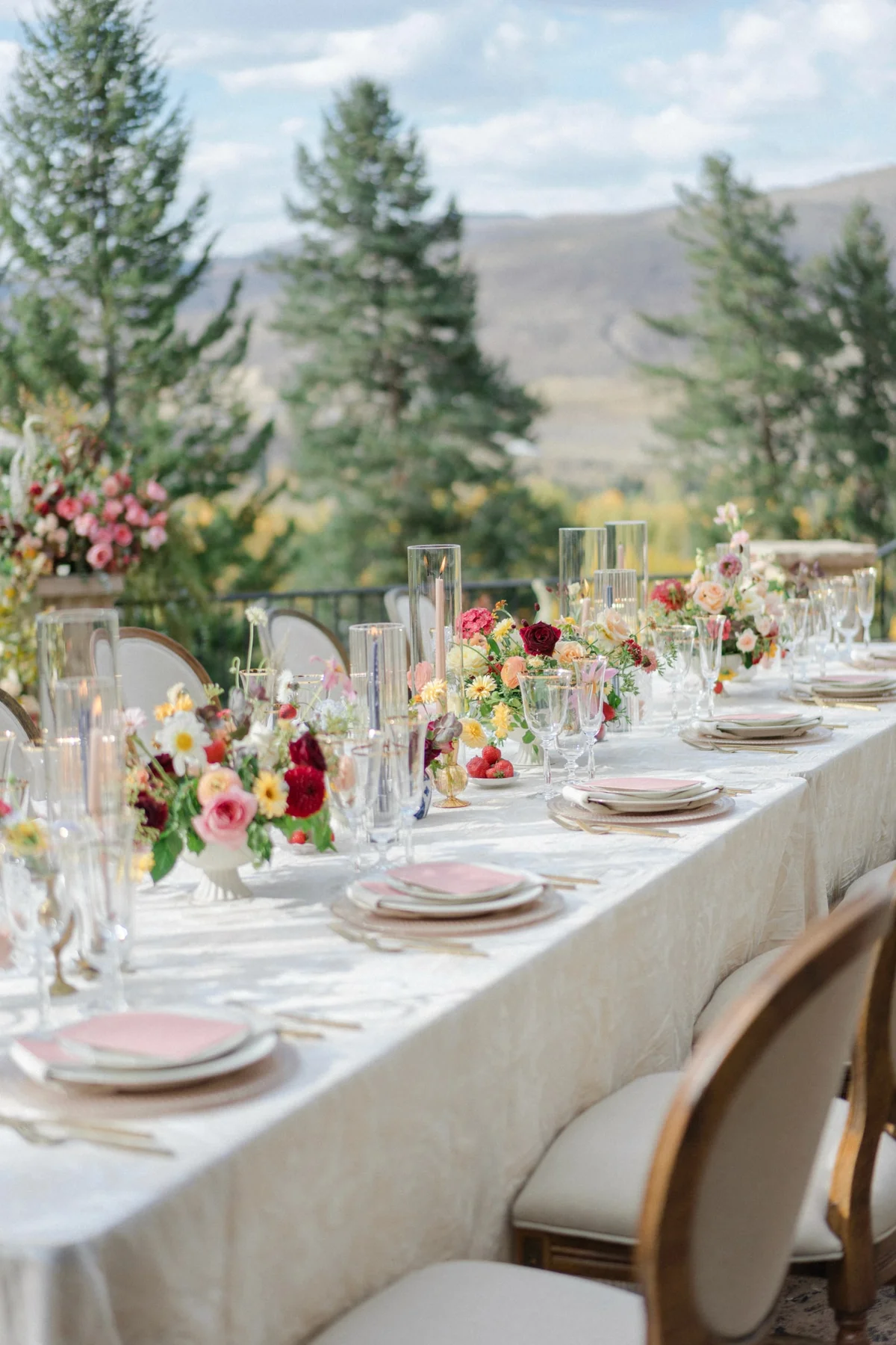 Outdoor reception table with flowers, glassware, and mountain scenery.