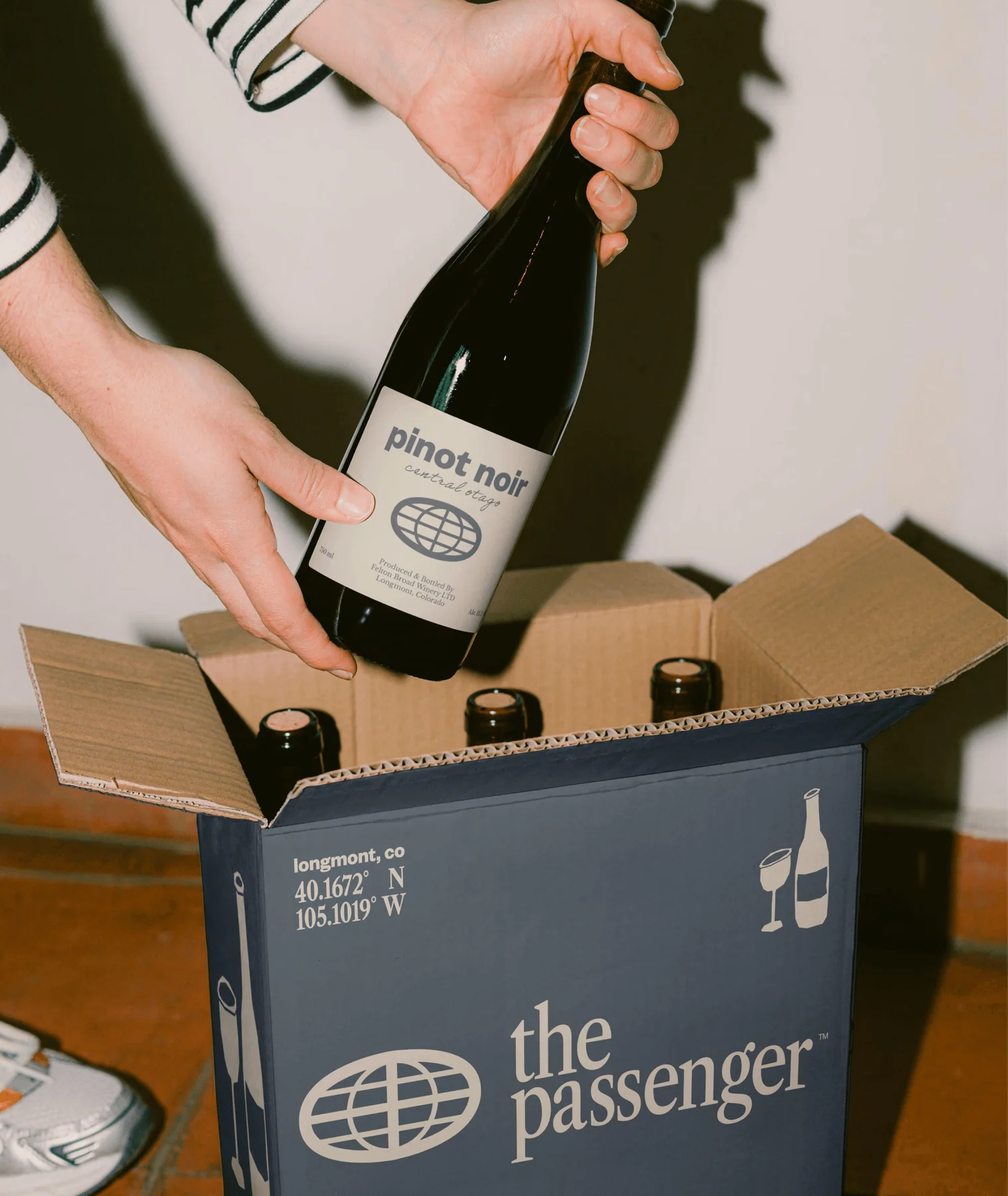Hands placing wine into a branded The Passenger cardboard carrier.
