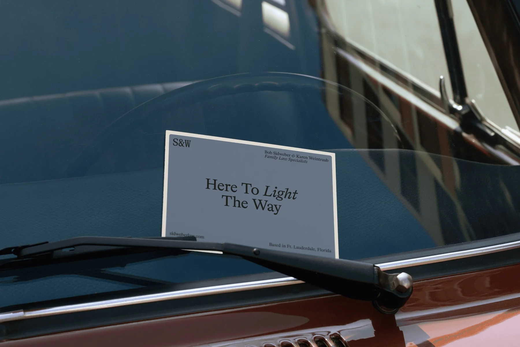 Printed S&W card reading Here To Light The Way behind a windshield.