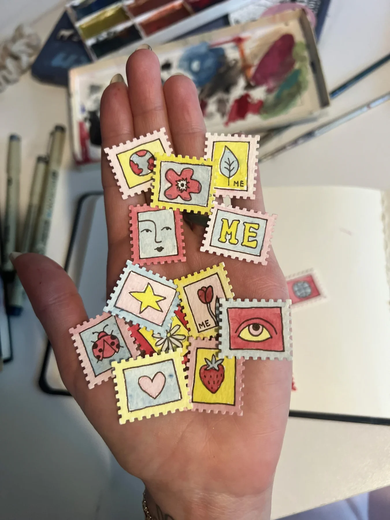 Hand holding colorful Molly Engels illustrated stamps.