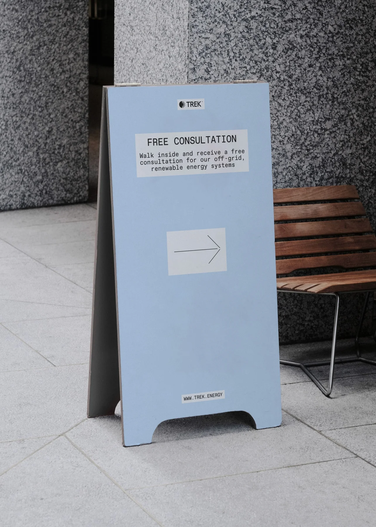 Pale blue Trek sidewalk sign with a directional arrow.