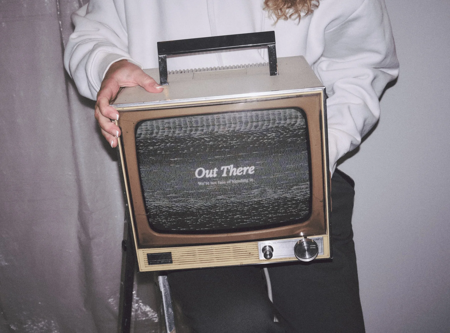 Person holding a vintage television displaying the Out There wordmark.