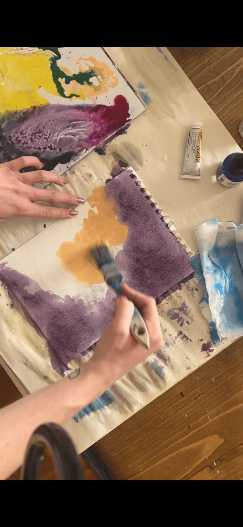 Hands working with watercolor paintings and art materials.