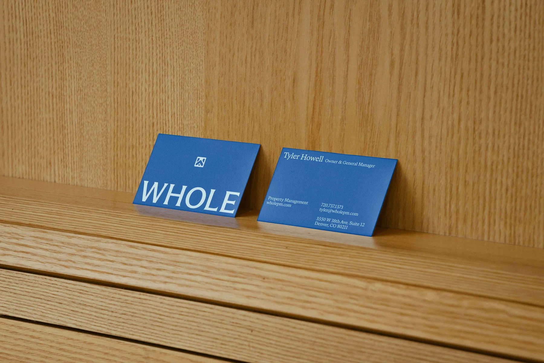 Two blue Whole business cards on a wooden ledge.