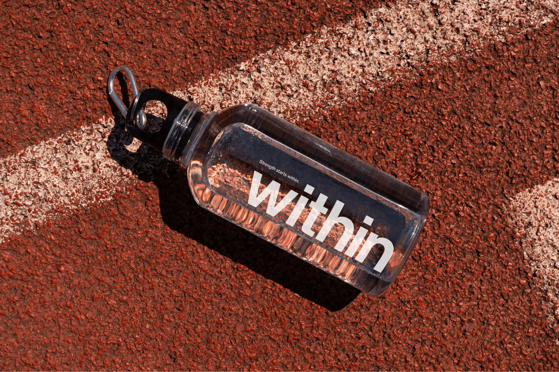 Clear Within water bottle resting on a red running track.