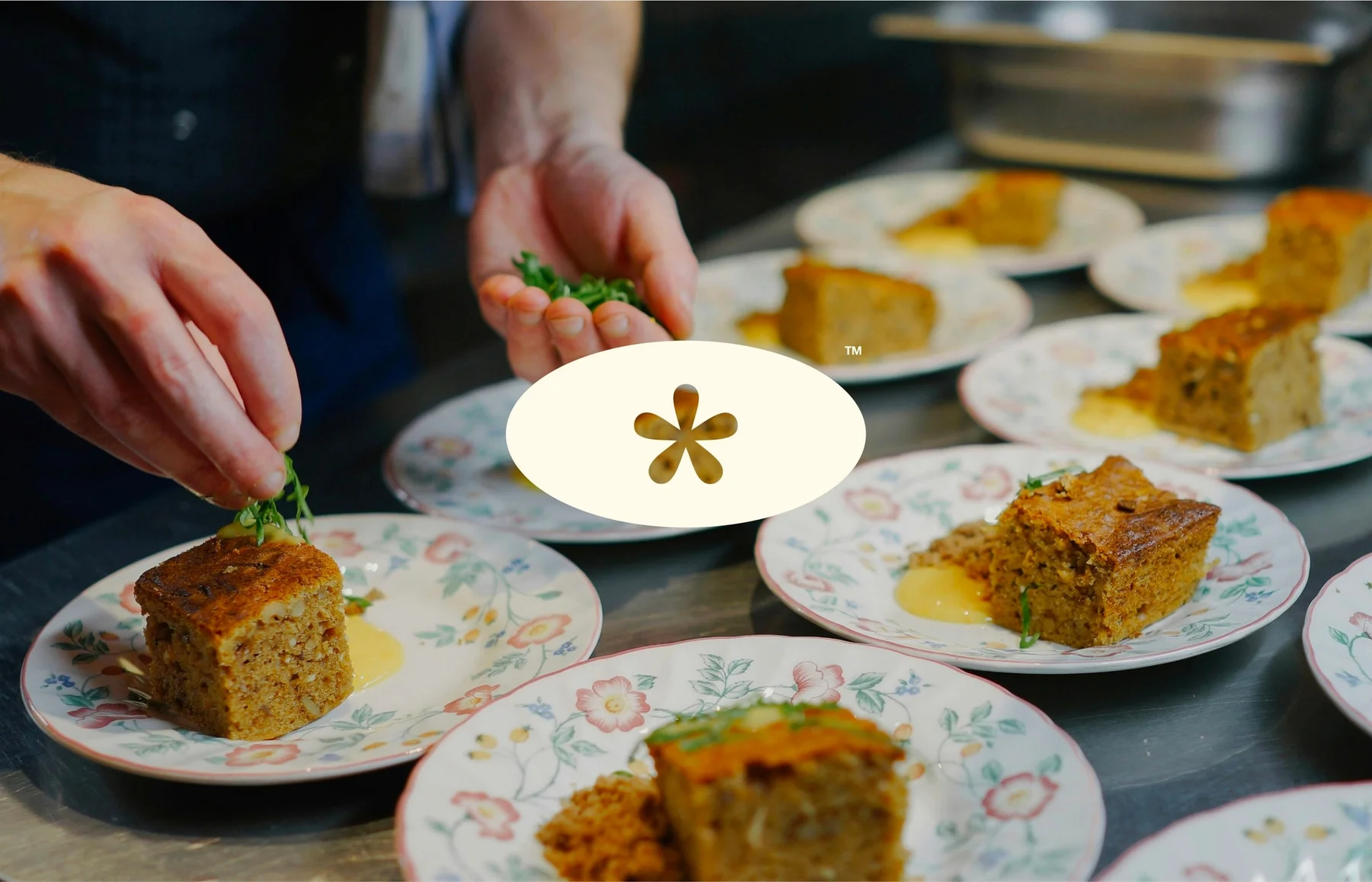 Hands finishing plated food with the Italic asterisk emblem overlaid.