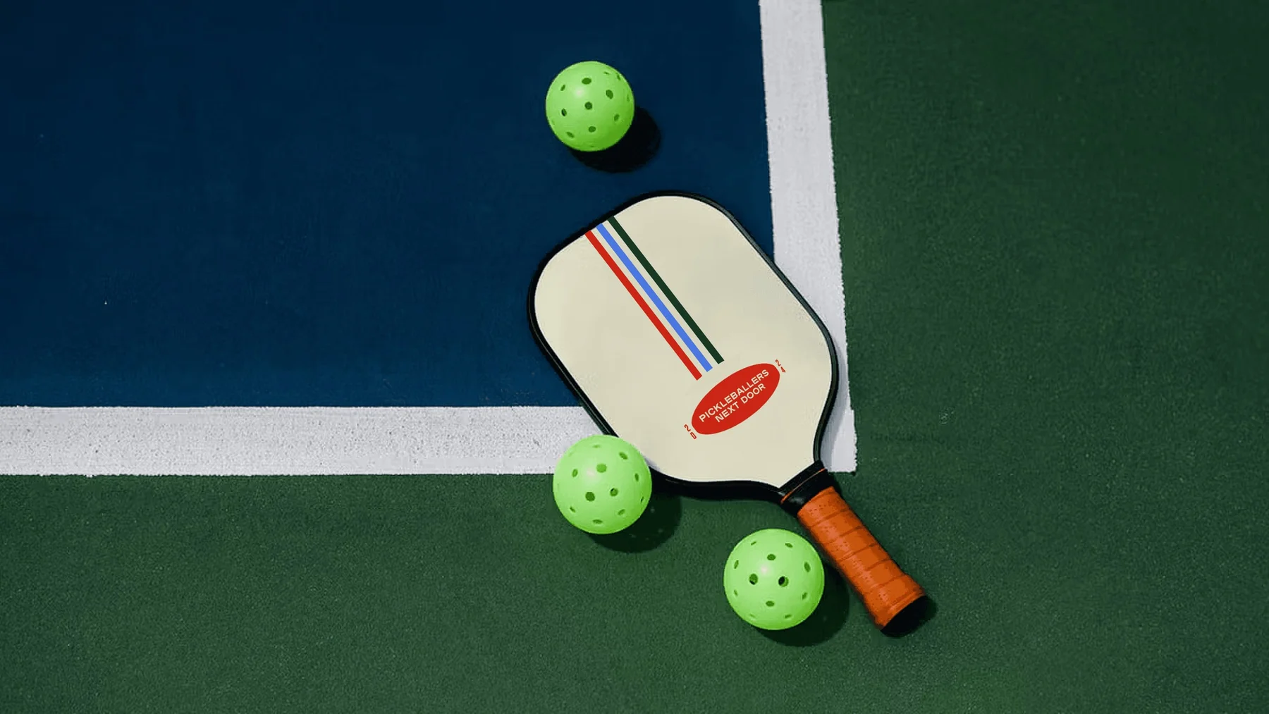 Cream pickleball paddle with colored stripes beside green balls on a court.