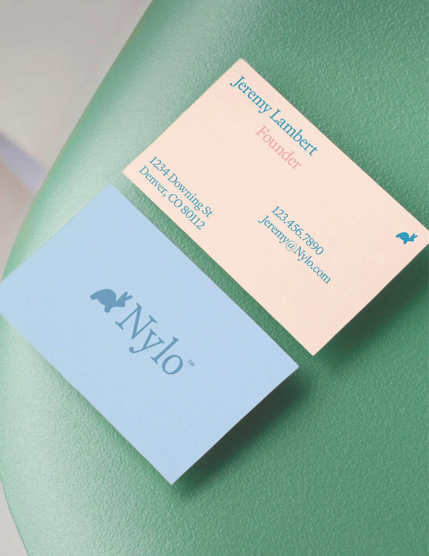 Peach and blue Nylo business cards on green upholstery.