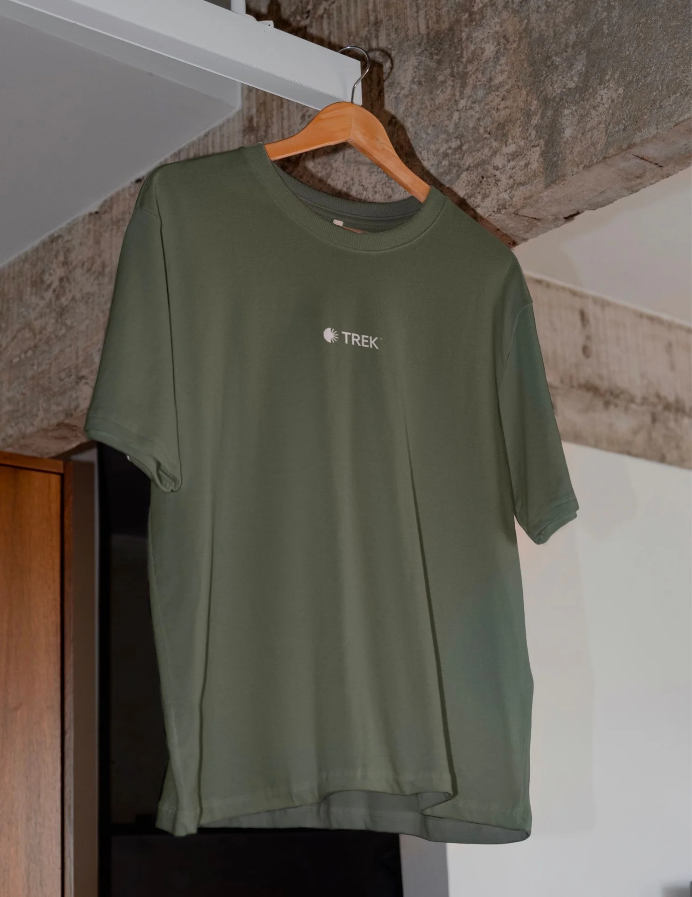 Green Trek T-shirt on a wooden hanger.