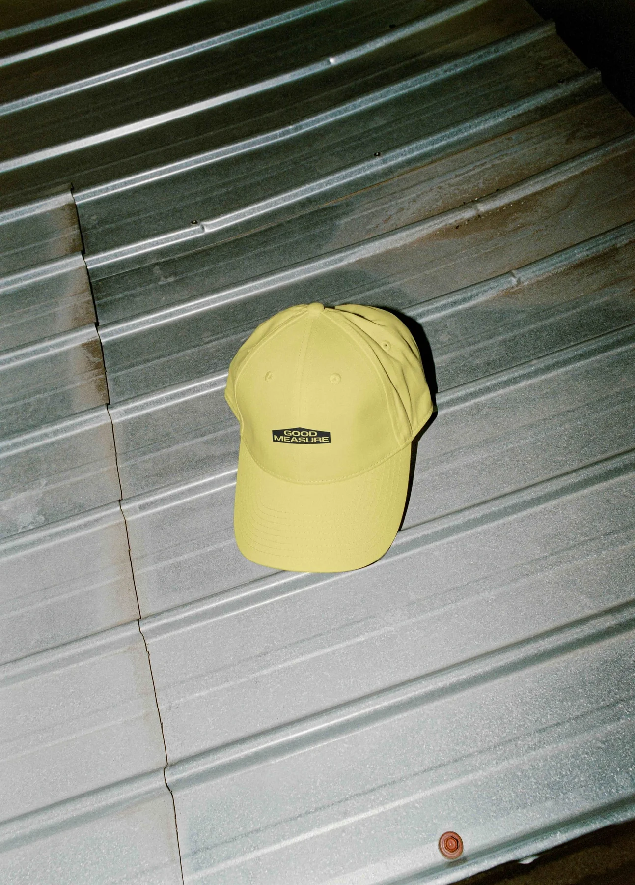 Yellow Good Measure cap hanging against a metal shutter.