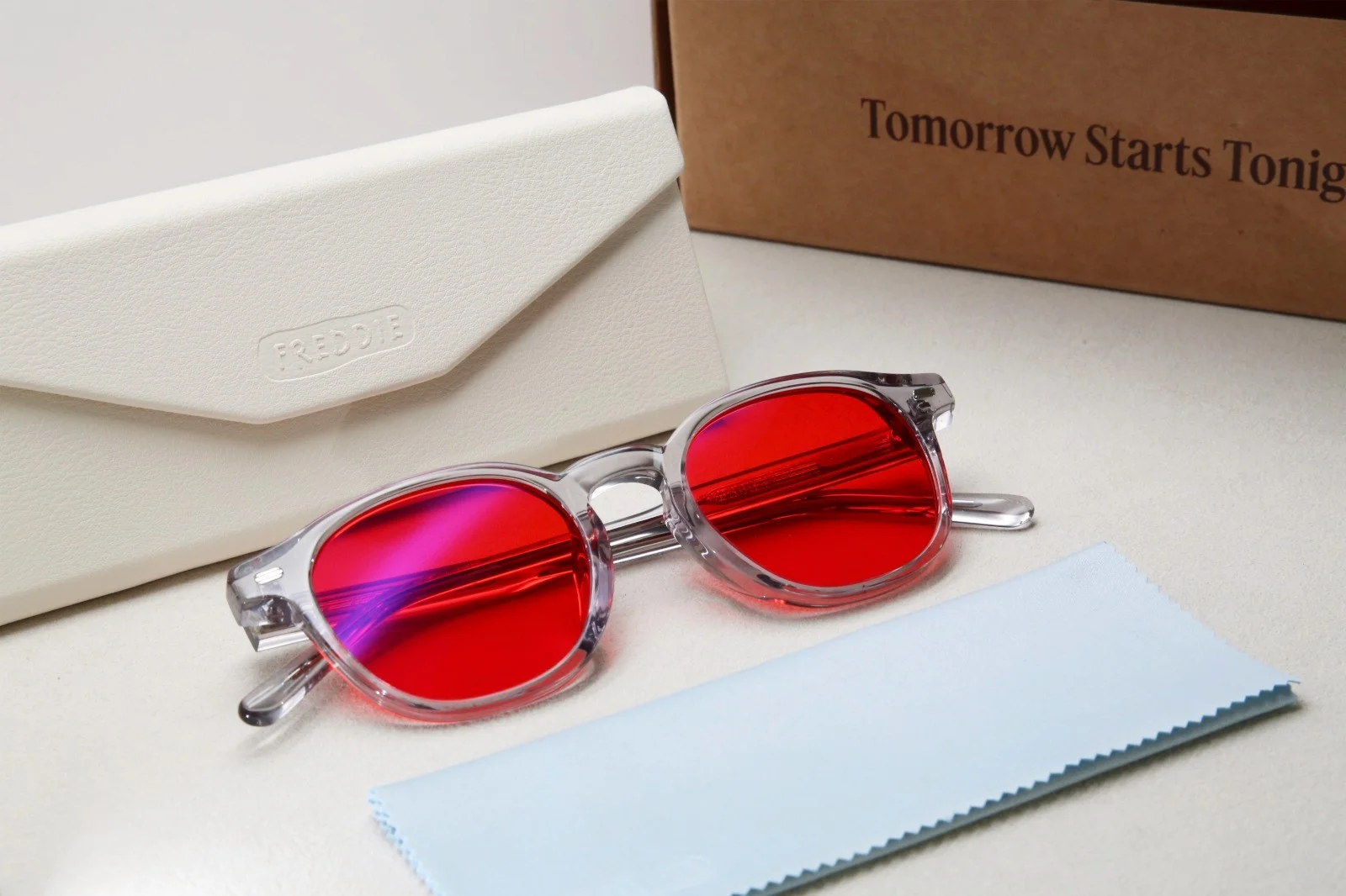 Red-lensed Freddie glasses with a case, cleaning cloth, and cardboard packaging.
