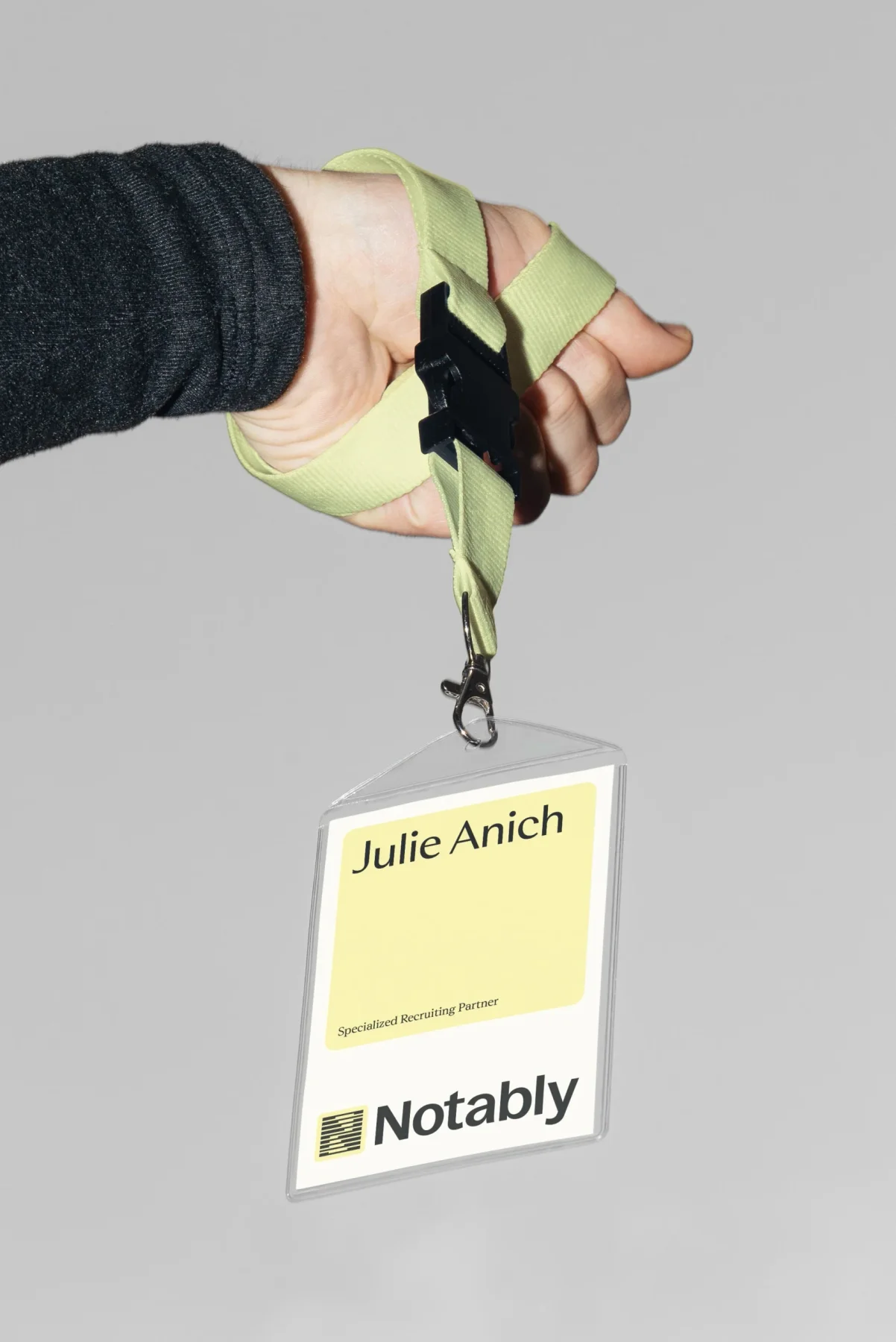 Hand holding a Notably badge on a pale yellow lanyard.