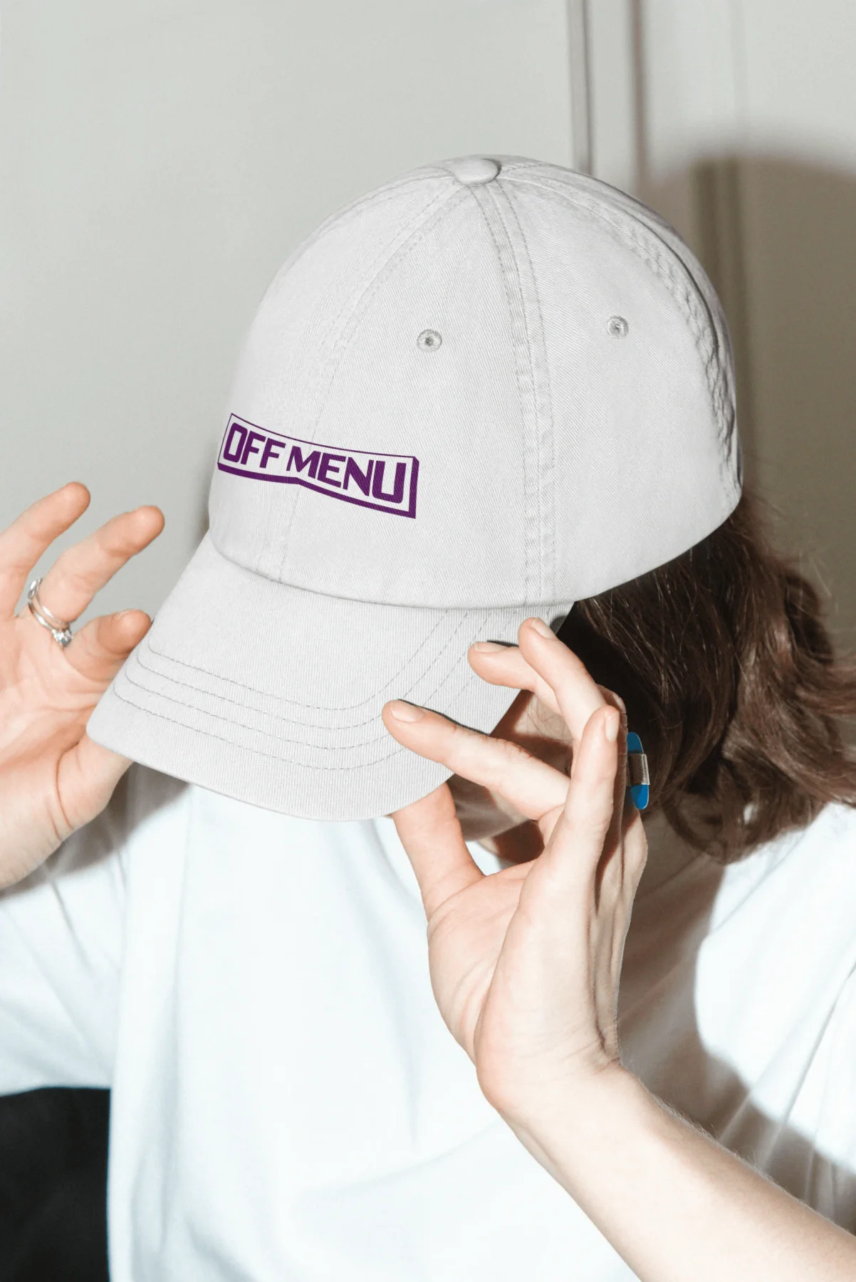 Person wearing a white cap embroidered with the purple Off Menu wordmark.